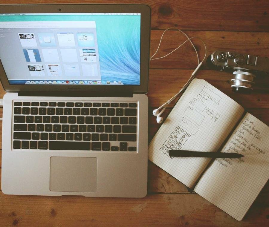 Laptop mit Website-Entwürfen und Notizbuch auf einem Holztisch